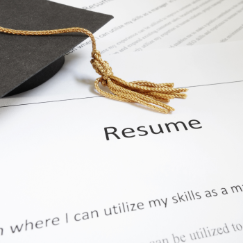 A small graduation cap on top of a resume.