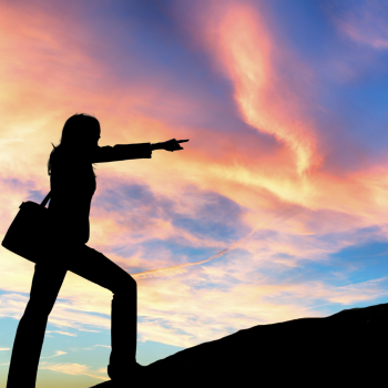 Silhouette of a business woman stepping up onto a hill and reaching forward against a colourful sunset sky.