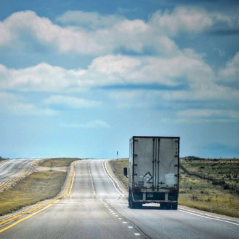 A semi-truck driving down a long road.
